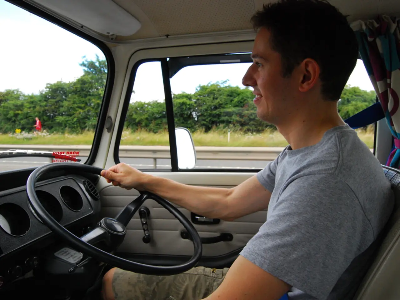 A person is driving a vehicle. He is wearing a grey t shirt and shorts. He is holding steering....