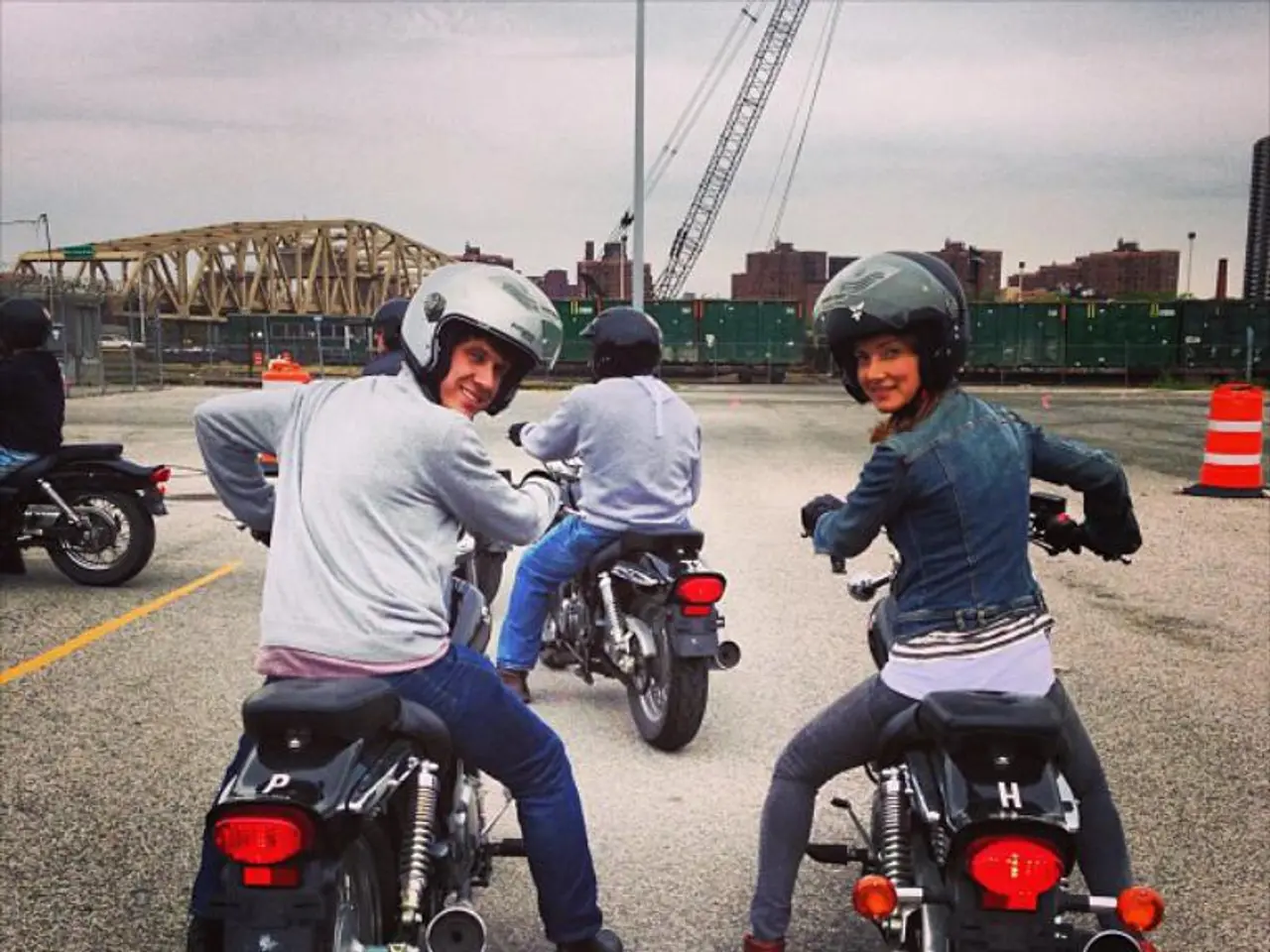 There are many people sitting on bikes wearing helmets. In the background there is a goods train,...