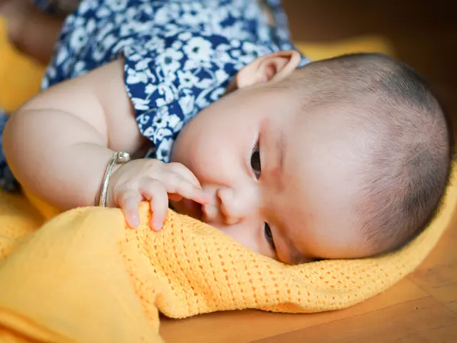 A baby wearing bangle is lying on a cloth and it is on another surface.