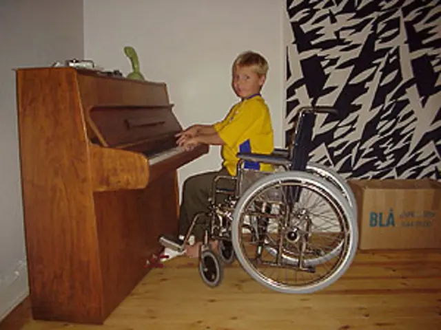 In this picture there is a boy is sitting on wheelchair and playing a piano. On top of piano there...