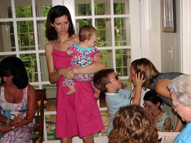 This woman is carrying a baby. Here we can see people. Through this glass windows we can see trees....